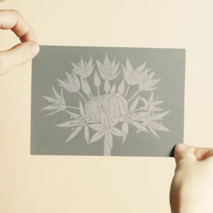 la linogravure représente une fleur d'ail des ours avec en son coeur la Cabane aux Herbes. l'encre utilisée est de couleur verte olive, un travail manuel signé l'Atelier du Lys.