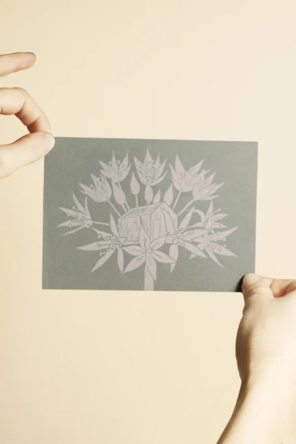la linogravure représente une fleur d'ail des ours avec en son coeur la Cabane aux Herbes. l'encre utilisée est de couleur verte olive, un travail manuel signé l'Atelier du Lys.
